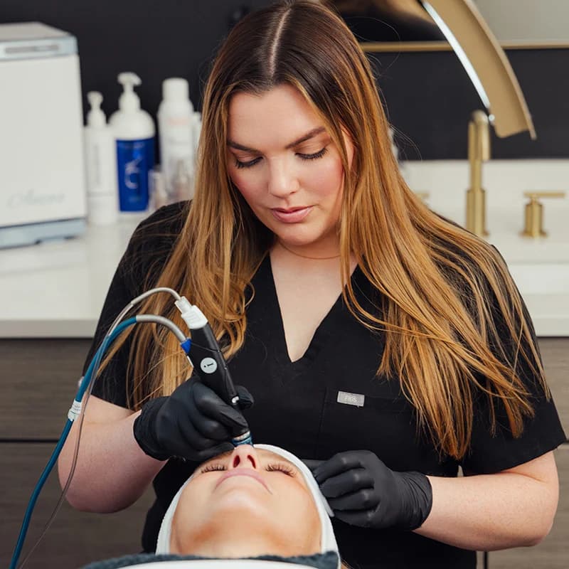 Esthetician performing a professional HydraFacial treatment on a client in a modern medical spa.